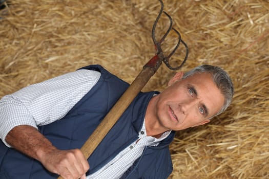 mature handsome farmer posing with fork against hay background