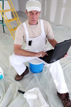 Painter sat on ladder with laptop