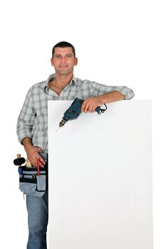 Builder with power drill stood by blank poster