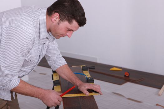 Man laying a floor and measuring a piece of wood