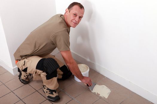 Man spreading adhesive over old floor tiles