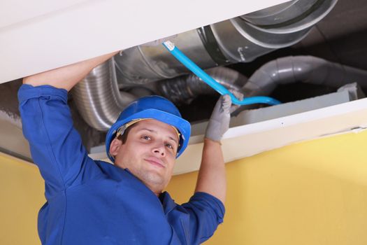 Plumber holding a blue pipe above a ceiling