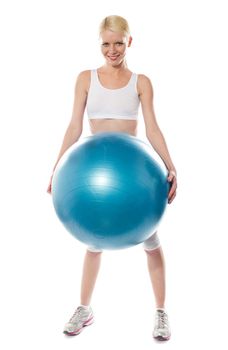 Smiling female athlete holding a big blue ball isolated over white