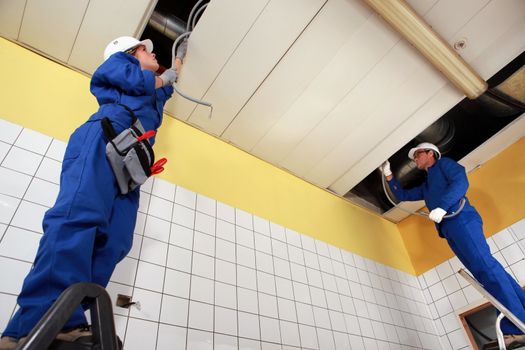 Two electricians repairing ceiling wiring