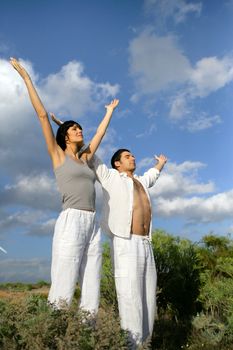 Couple stood in a field with their arms raised