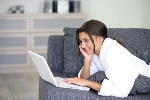Woman lying on a sofa and using her laptop