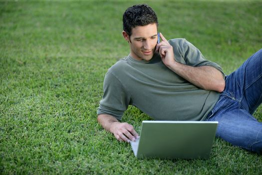 Relaxed man using phone and computer laid on the grass