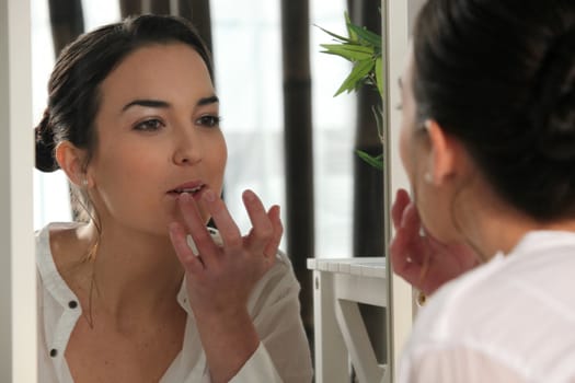 Woman applying lip gloss in a mirror