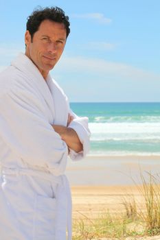 Man in a bathrobe standing on a sandy beach