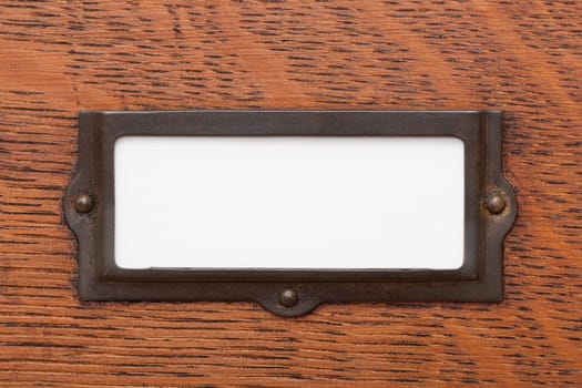 Close up of a blank, white label in an old brass label holder on an oak filing cabinet drawer.