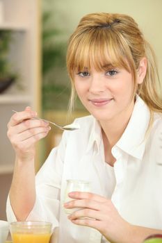 Young woman eating yoghurt at breakfast