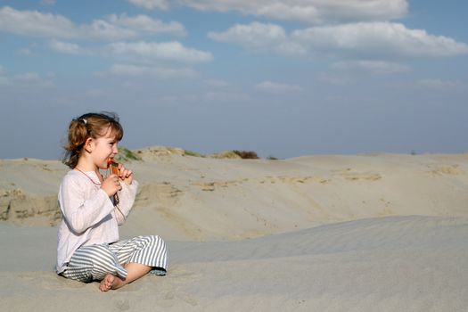 little girl sitting on sand and play music