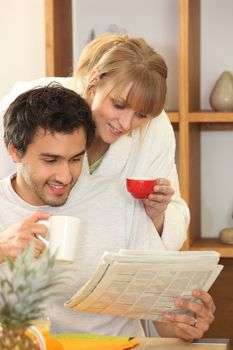 Couple drinking coffee and looking at a newspaper together