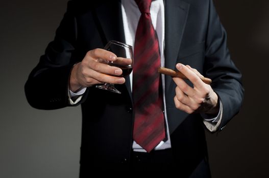 man in a business suit holds a cigar and a glass with whisky