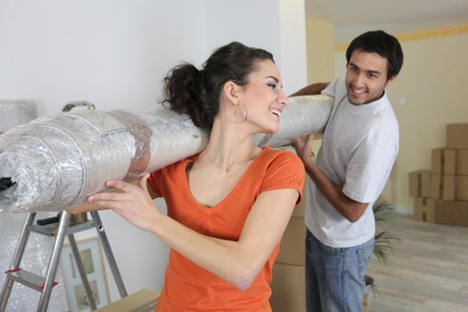 Couple carrying new rolled-up carpet in to house