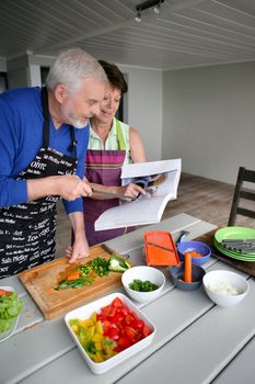 Elderly couple preparing a meal with the help of a cookbook