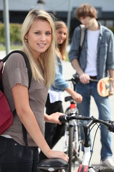 Blond female teenager stood by bicycle friends in background