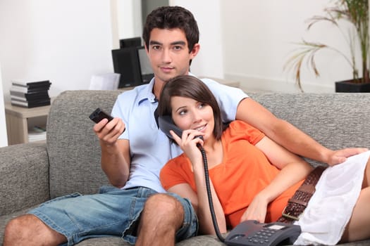 Young couple at home, watching TV and talking on the telephone