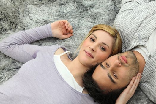 Young couple lying top to tail on a grey carpet