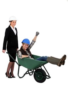 Architect pushing her colleague in wheelbarrow