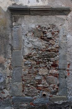 Old window in gray stone wall blocked by bricks and stones