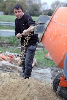 Labourer shovelling gravel into a mixer