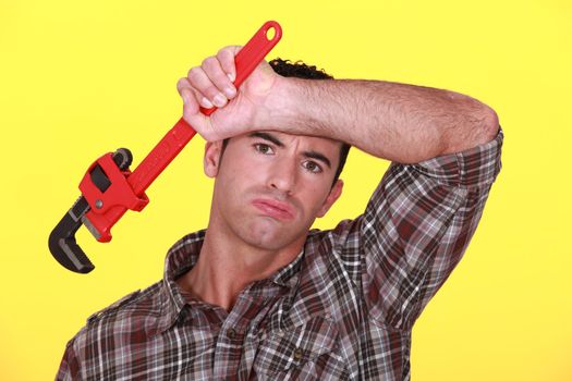 exhausted craftsman with adjustable spanner against yellow background