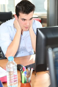Young man holding his neck in front of a desktop computer
