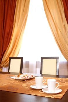 on a table there are two white coffee cups and a plate with candies