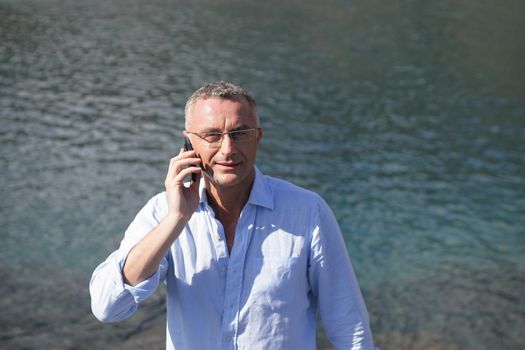 Businessman with a cellphone in front of water