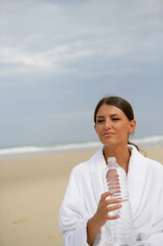 Brunette stood on a beach holding bottle of water