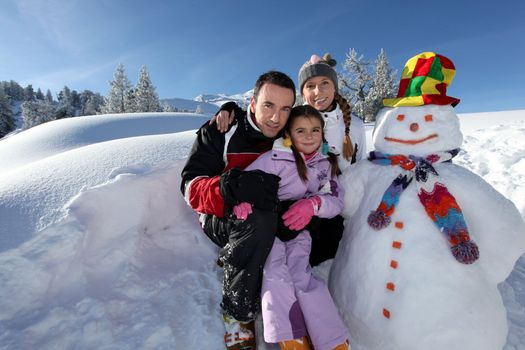 couple posing with child beside snowman at mountain resort