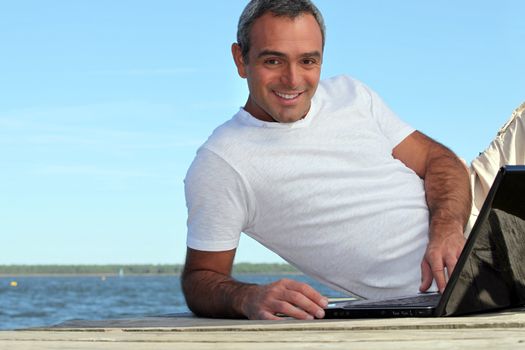 Man looking his laptop by the lake