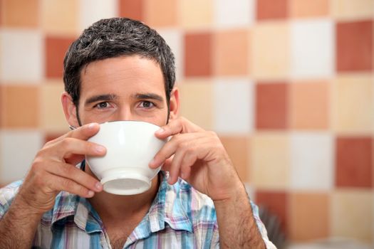 Man drinking from a white bowl in a tiled kitchen