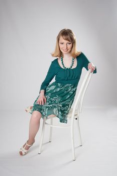 Blonde in a green dress sitting on a white chair.