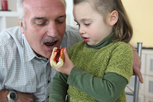 Granddaughter giving her grandfather a piece of bread with jam to eat