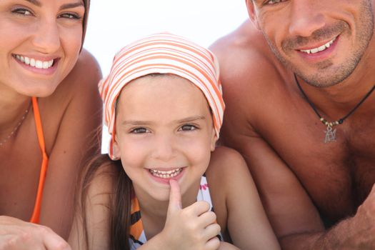 Young girl lying between her parents on the beach