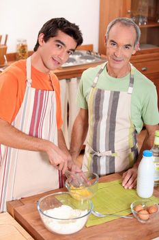 a young man and his grand father wearing aprons and making a cake