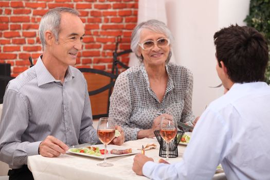 Young man and senior couple having a dinner in a restaurant