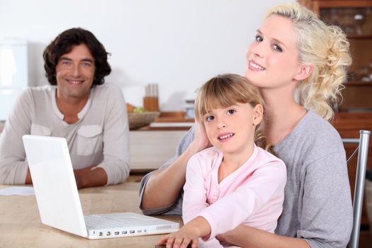 parents and her daughter smiling in the kitchen, a computer is on the table