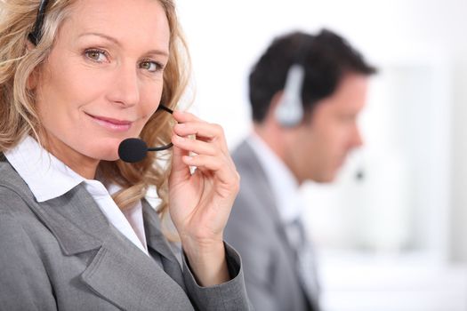 Woman in a suit using a headset with a male colleague in the background