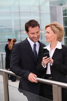 Businessman and businesswoman watching mobile phone outdoors
