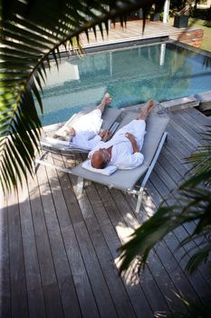 Elderly couple on sunloungers by a pool