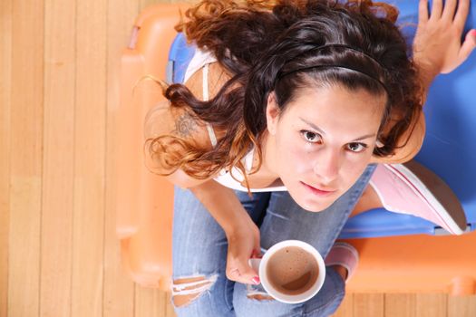 A young woman sitting on a stack of suitcases while drinking coffee and waiting for the departure to vacations.