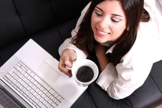 A young, hispanic adult girl watching a Laptop while drinking coffee.