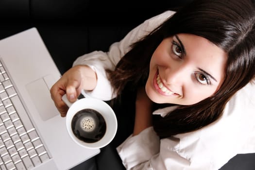 A young, hispanic adult girl with a Laptop and drinking coffee.