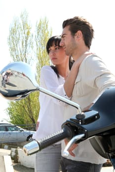 Couple standing next to a parked scooter