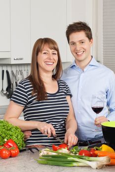 Photo of a young couple preparing salad in their kitchen and drinking wine.