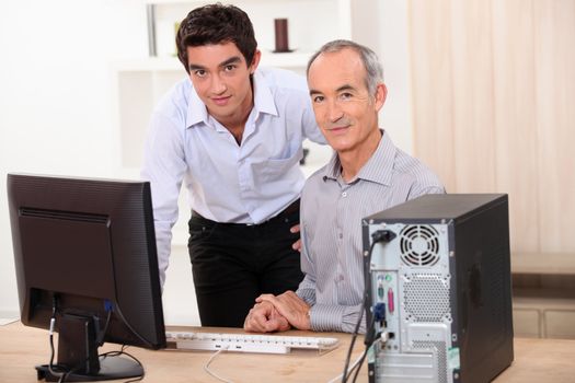 a young man and a senior man behind a computer