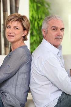 Mature couple sitting back to back at home